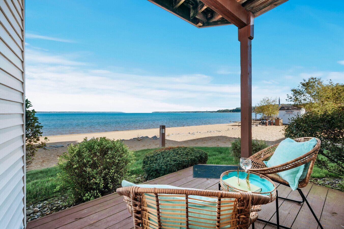 Eine Holzterrasse mit Korbstühlen und einem Weinglas, mit Blick auf einen Strand und den Ozean.