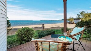 A wooden deck with wicker chairs and a glass of wine, overlooking a beach and the ocean. - Sauna Beach Haven 106 Direct Beach Access Near Downtown Tart Trail (Traverse City)
