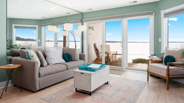 A living room with a sofa, a coffee table, and a chair. There is a large window with a view of the beach. - Sauna Beach Haven 106 Direct Beach Access Near Downtown Tart Trail (Traverse City)