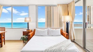 Habitación de hotel con una cama grande, dos mesitas de noche, un escritorio y vistas al océano.
