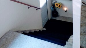 A staircase with a dark riser, a white handrail, and a small shelf with a vase of flowers. - The Hideout (Crescent City)