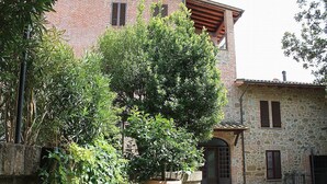 Ein Innenhof mit einem großen Kübelbaum, einer Steinmauer und einem Gebäude mit einer Fassade aus Stein und Holzläden.