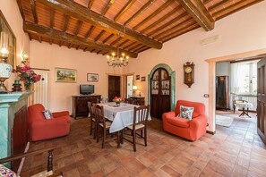 A cozy living room with a wooden ceiling, a dining table with chairs, a red sofa, and a television.