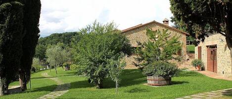 A stone building with a red roof, surrounded by a well-maintained lawn and trees.
