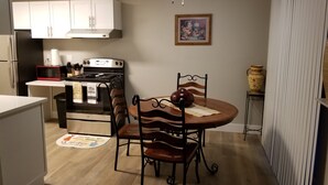 Una cocina compacta con armarios blancos, microondas, estufa y una mesa de comedor con sillas.