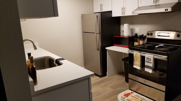 Una cocina compacta con armarios blancos, un refrigerador de acero inoxidable, un microondas y una estufa.