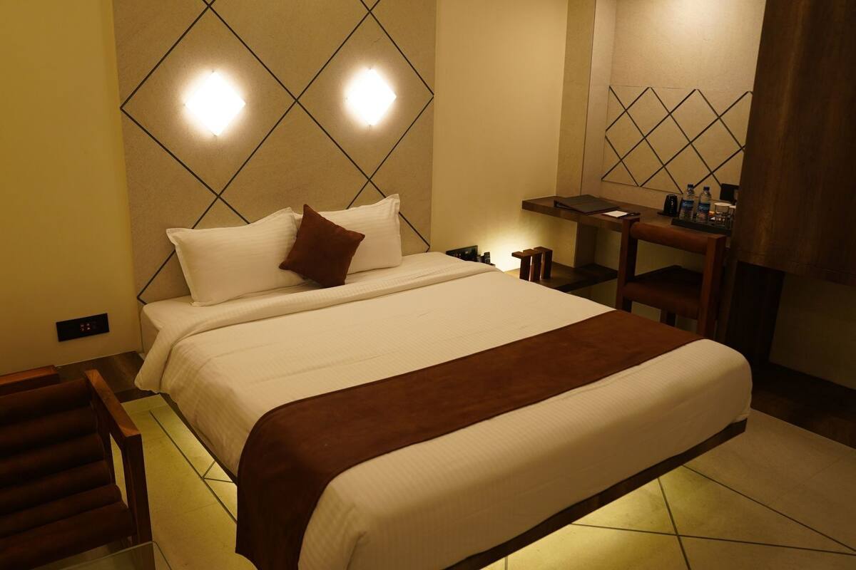 A hotel room with a bed, bedside table, and a wall-mounted light fixture.