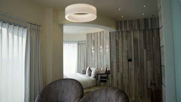 Et moderne hotelværelse med en stor seng, et siddeområde med sofa og lænestole, en trævæg og en stor, rund lampe.
