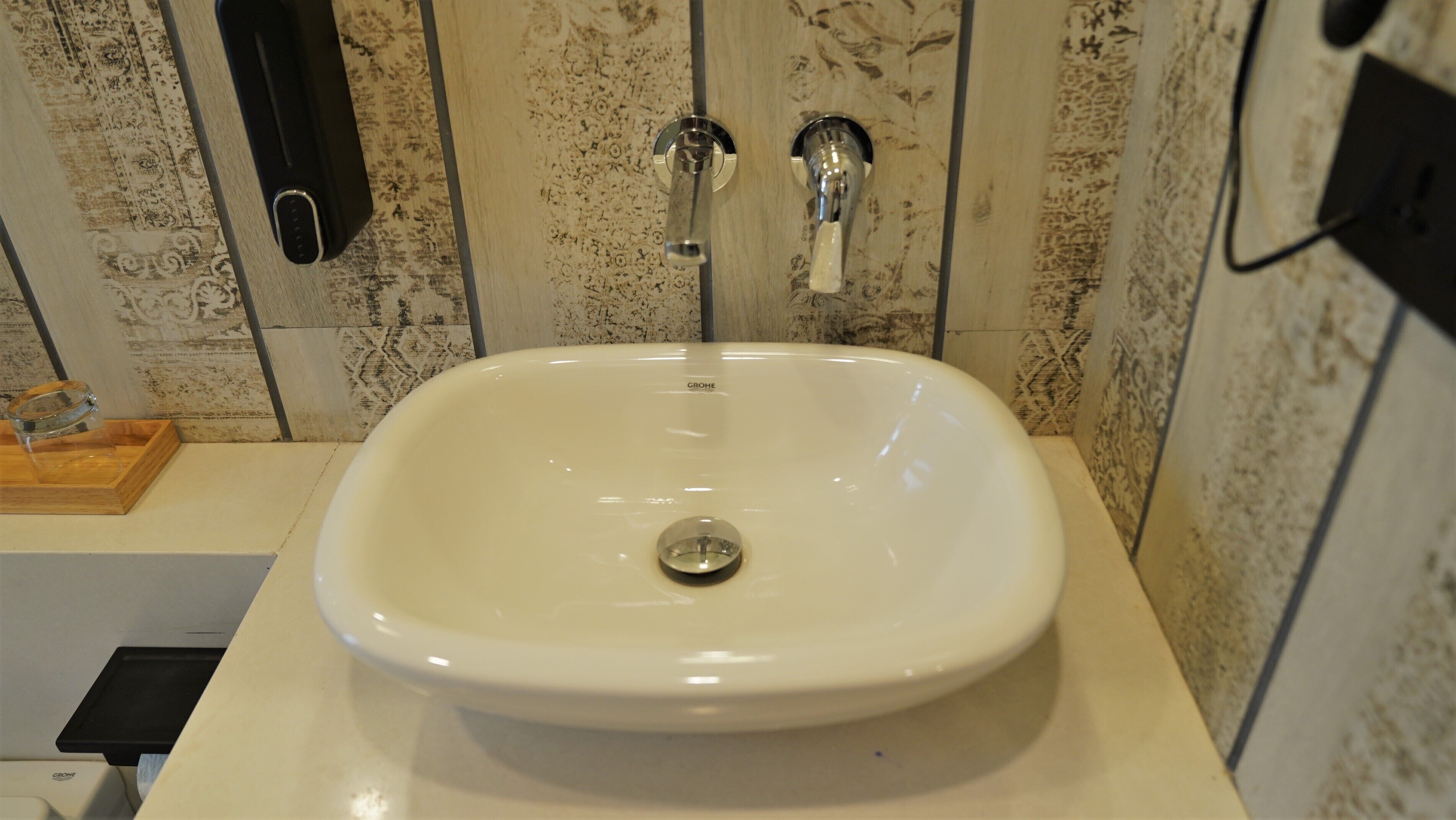 A bathroom with a white sink, two faucets, and a wooden tray.