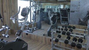 Et fitnessrum med træningsudstyr, herunder løbebånd og håndvægte, samt et spejl der afspejler rummet.