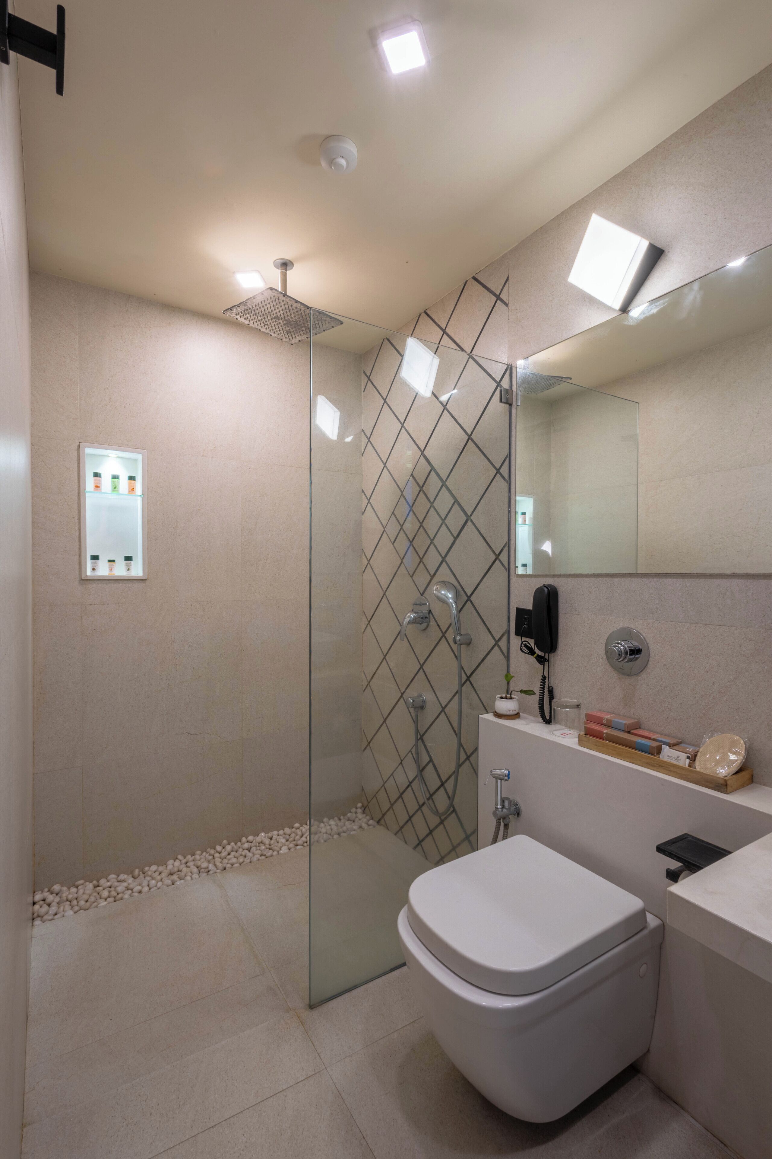 Une salle de bain moderne avec une douche à parois de verre, des toilettes blanches, un meuble-lavabo avec un miroir et une petite étagère contenant des articles de toilette.