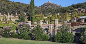 Une propriété située sur une colline, avec des bâtiments en pierre recouverts de végétation, un arbre imposant et une montagne en arrière-plan.