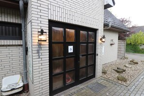 Ein Gebäude mit Ziegelaußenwand, einer großen Glastür mit vielen Glasscheiben und zwei Wandleuchten.