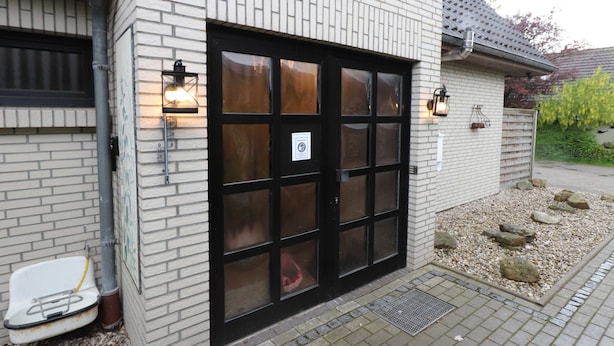 Ein Gebäude mit Ziegelaußenwand, einer großen Glastür mit vielen Glasscheiben und zwei Wandleuchten.