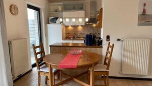 A compact kitchen with a dining area, featuring a wooden table and chairs, a microwave, and a coffee maker. - Ferienwohnungen Jade-blick, WH EG Rechts (Varel)