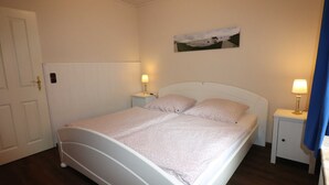 A neatly made bed with a white headboard, two bedside tables with lamps, and a painting on the wall. - Ferienwohnungen Jade-blick, WH EG Rechts (Varel)