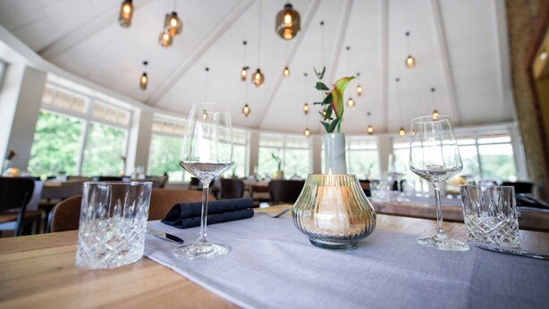 Een eetgedeelte met tafels gedekt voor twee personen, helder servies en hangende hanglampen.