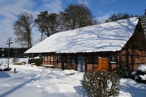 A traditional wooden building with a snow-covered roof, a wooden bench, and a small garden area.