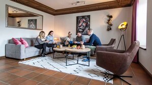 Een woonkamer met een grijze bank, een ronde salontafel, een bruine fauteuil en een vloerlamp.