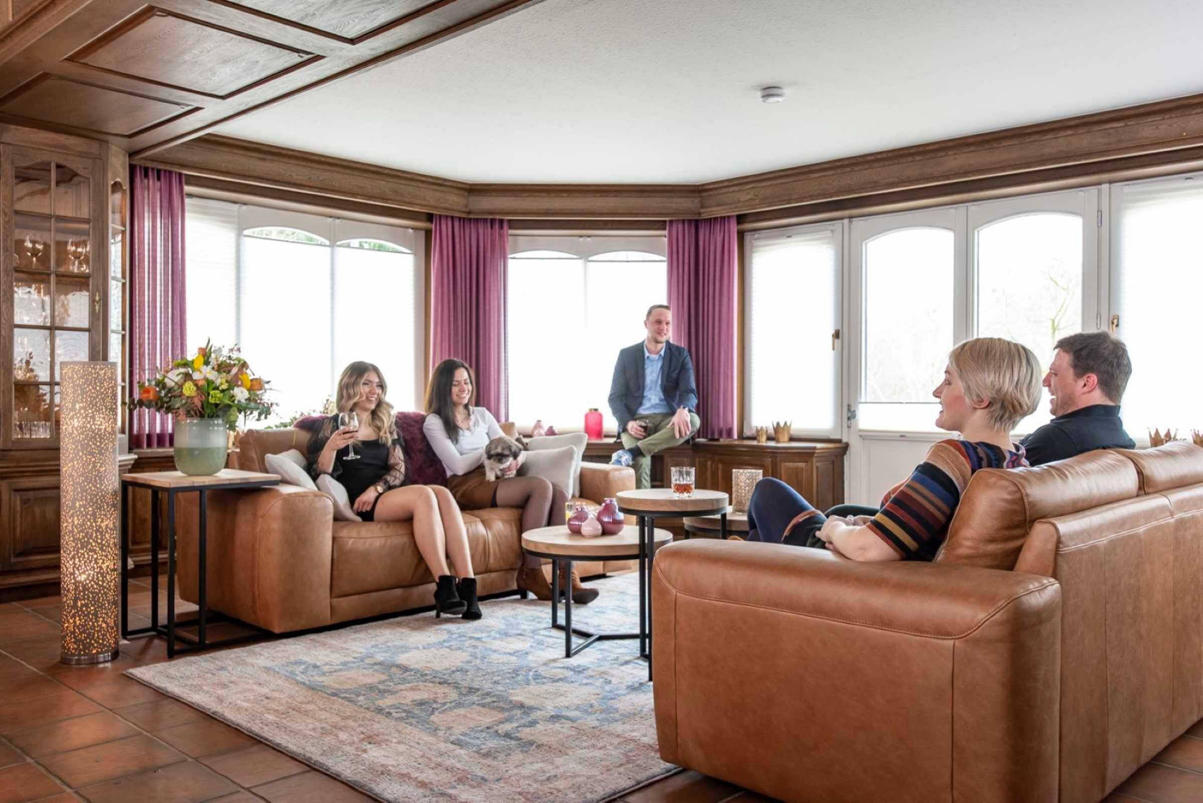 Een ruime woonkamer met leren banken, een salontafel en een groot raam met gordijnen.