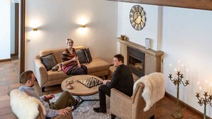 Een ruime woonkamer met een hoge nok, houten balustrade en een open haard.