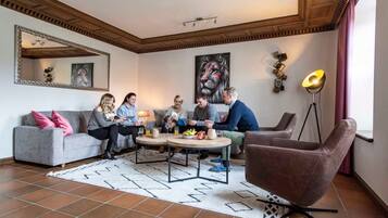 Een woonkamer met een grijze bank, een ronde salontafel, een bruine fauteuil en een vloerlamp.