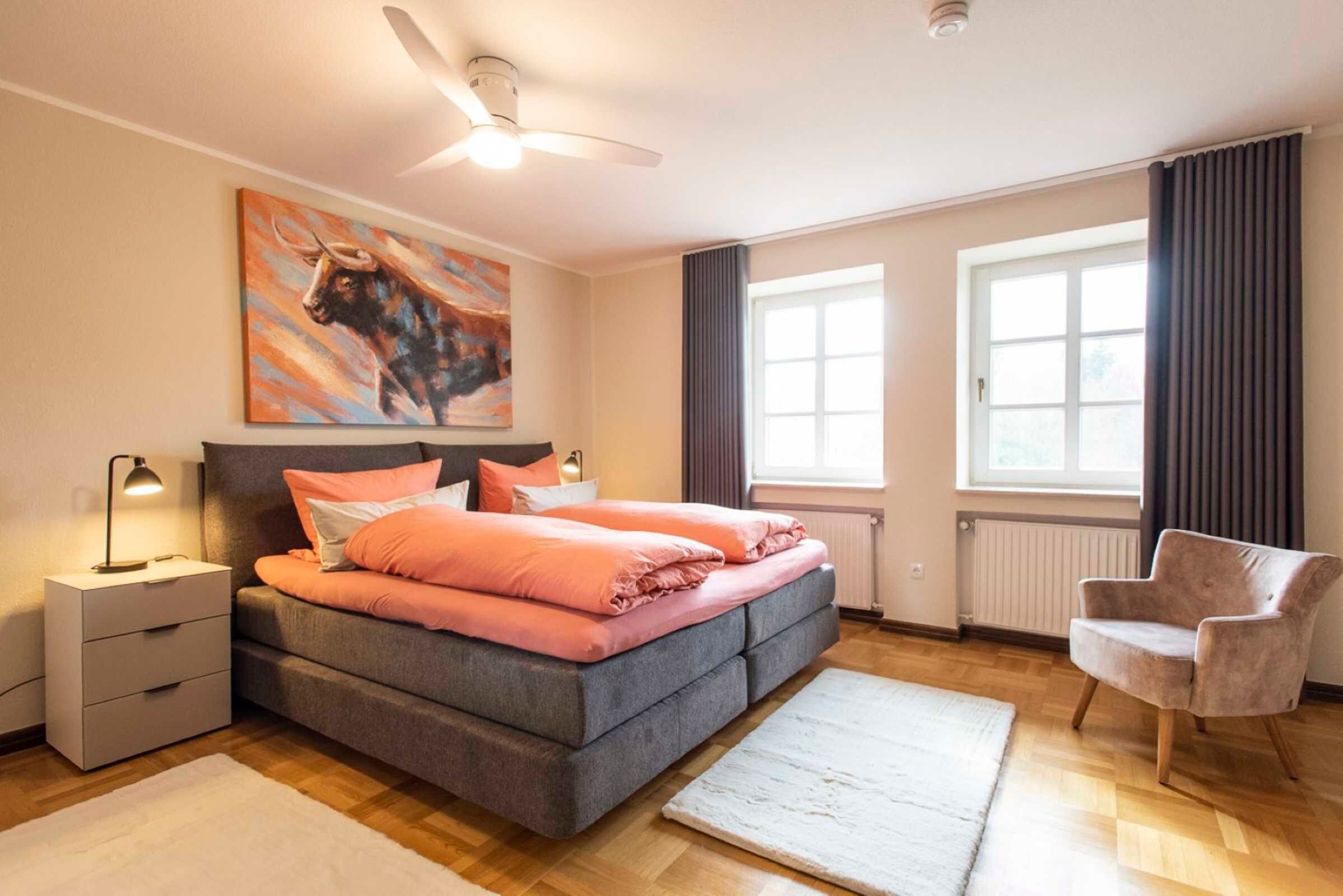 Una camera da letto con un letto, comodini, una sedia, una ventola a soffitto e una finestra.