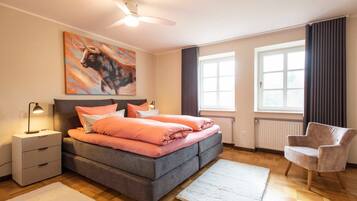 Una camera da letto con un letto, comodini, una sedia, una ventola a soffitto e una finestra.