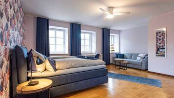 A modern bedroom with a large bed, a small table, a sofa, and a ceiling fan.