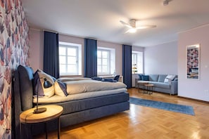 A modern bedroom with a large bed, a small table, a sofa, and a ceiling fan.
