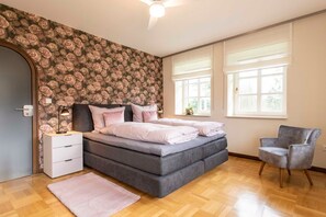 A bedroom with a bed, a chair, a nightstand, a dresser, and a window.