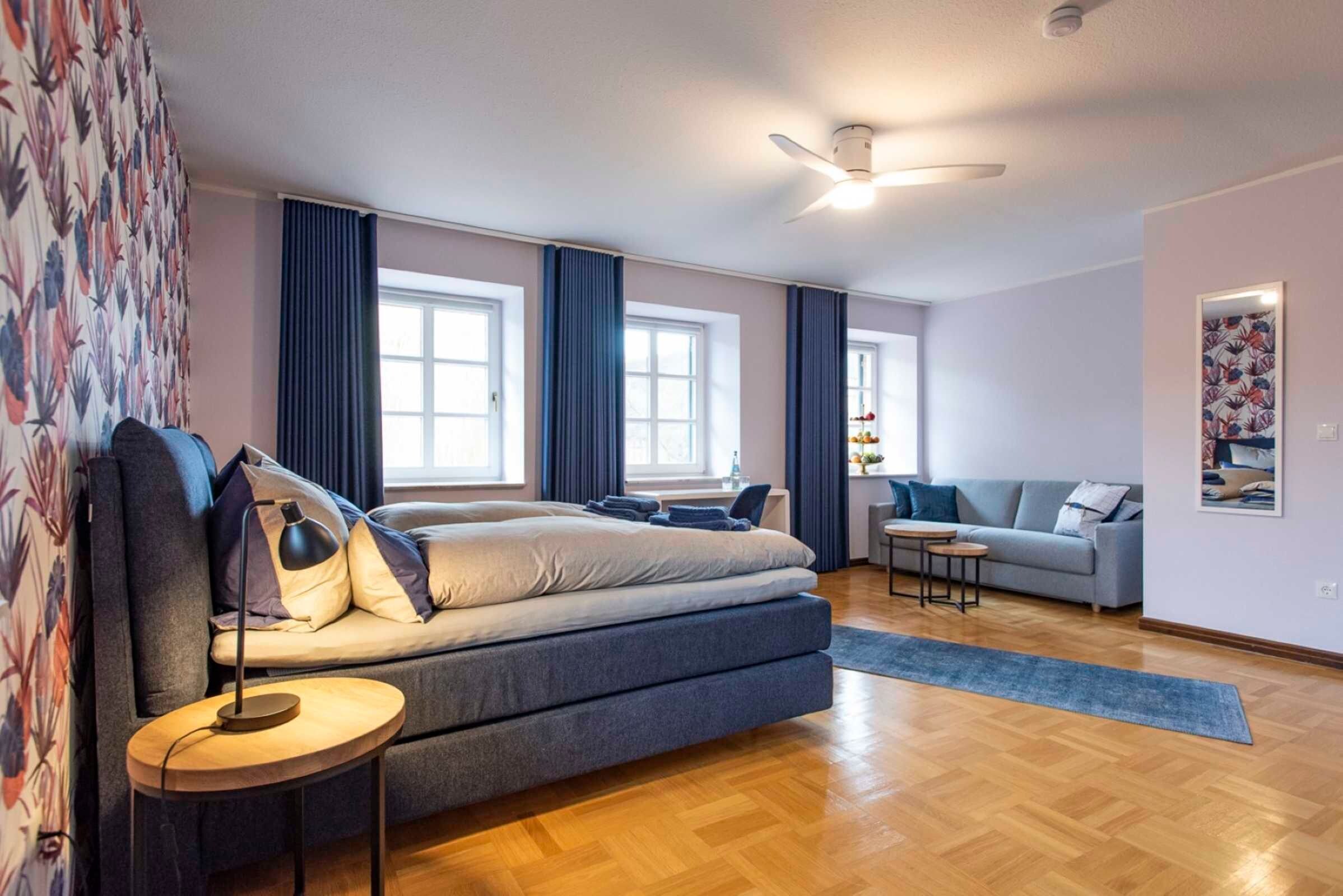 Ein modernes Schlafzimmer mit einem großen Bett, einem kleinen Tisch, einer Couch und einem Deckenventilator.