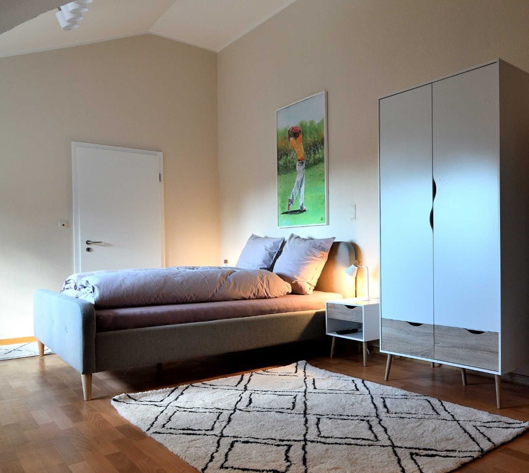 Une chambre à coucher avec un lit, une table de chevet, une lampe, une armoire et un tableau au mur.