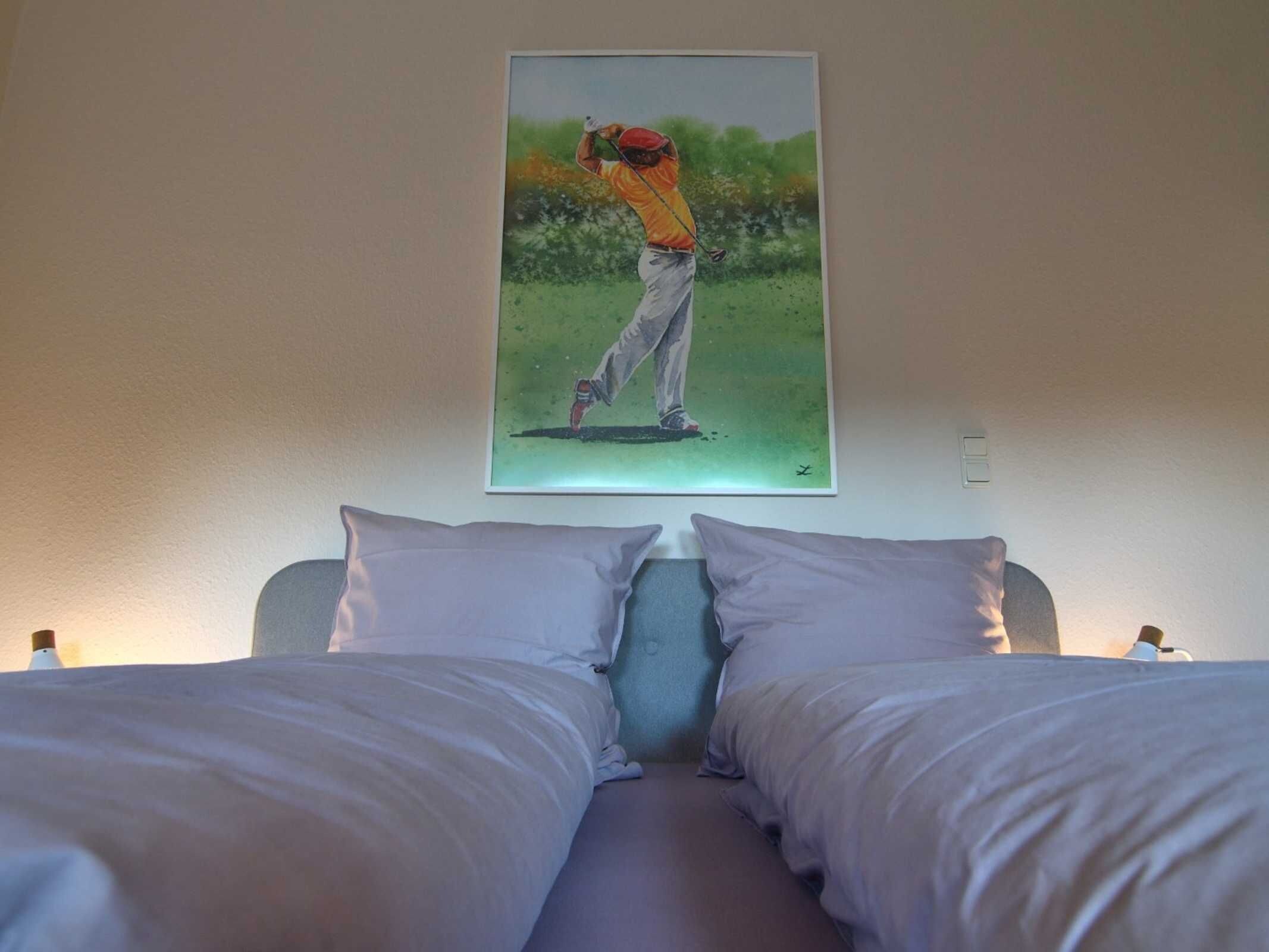 Un dormitorio con dos camas, un cuadro de un golfista y una luz nocturna.