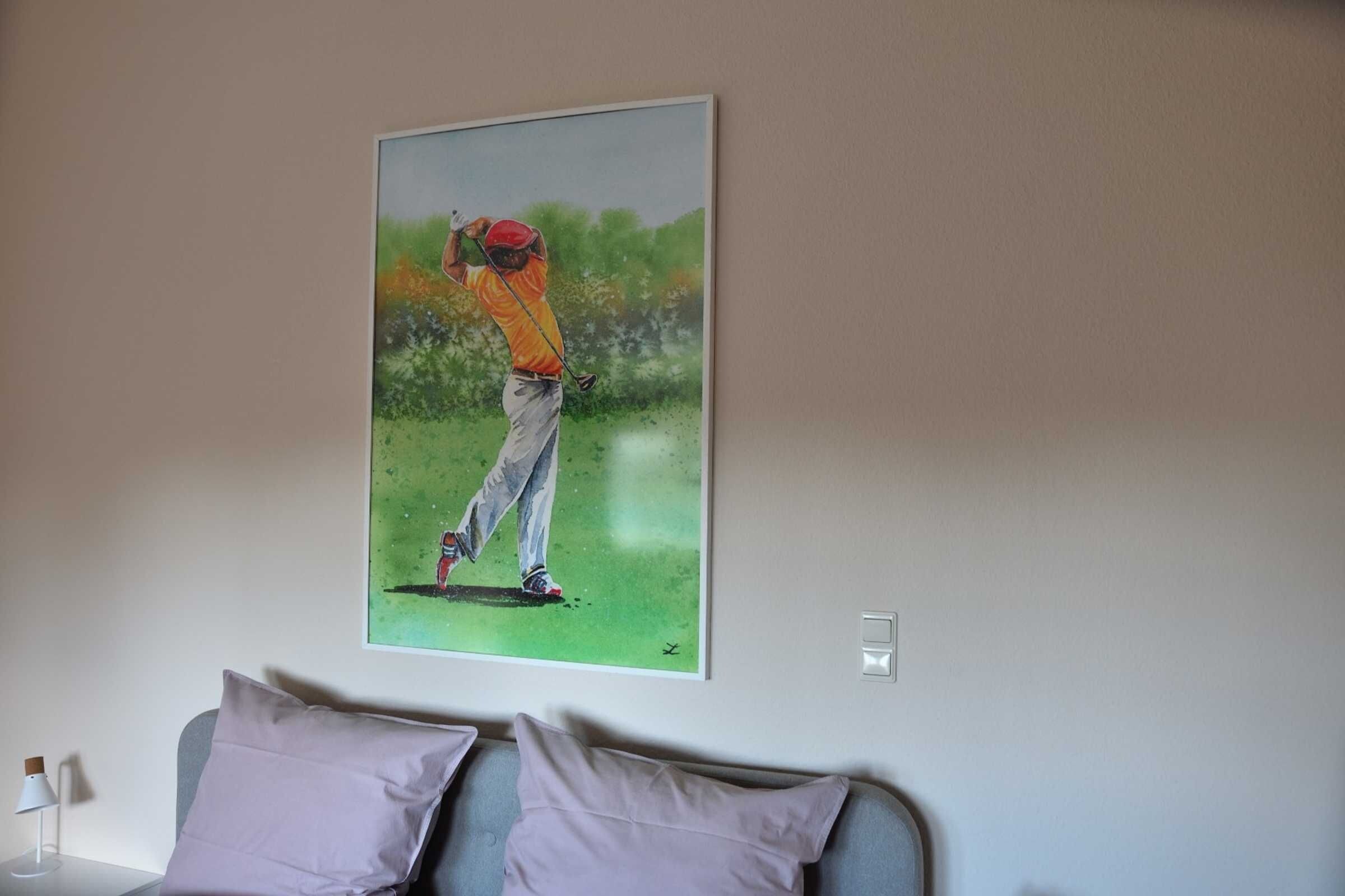 Un dipinto raffigura un golfista su un manto erboso, un divano grigio e una parete bianca.