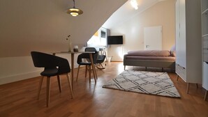 A small, modern apartment with a dining area, a sofa, a TV mounted on the wall, and a wooden floor. - Appartement Crows Nest - Crow´s Nest (Ankum)