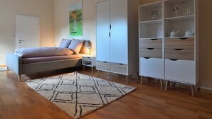 A bedroom with a bed, a nightstand, a lamp, a wardrobe, and a shelf with glassware. - Appartement Crows Nest - Crow´s Nest (Ankum)