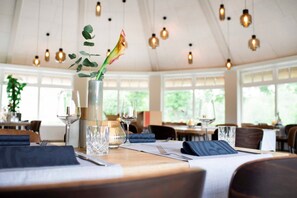 A dining area with tables set for two, a vase with a plant, and hanging pendant lights. - Appartement Crows Nest - Crow´s Nest (Ankum)