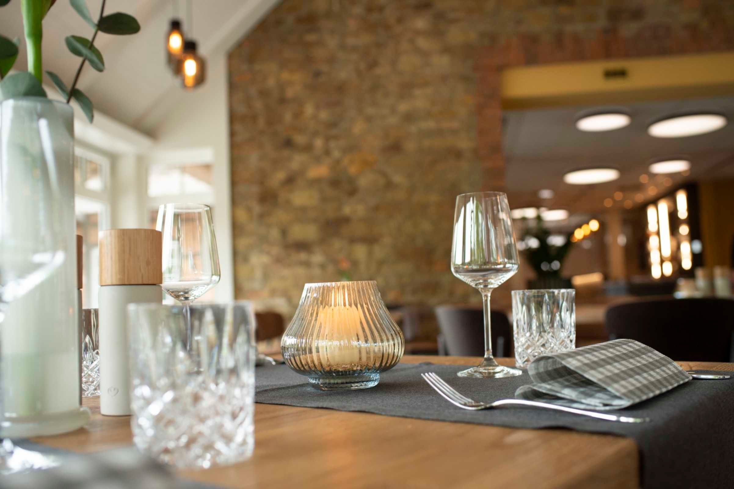 Un ambiente de restaurante con una mesa lista para comer, que incluye una vela, una copa de vino y cubiertos.