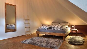 A loft bedroom with a sloped ceiling, a wooden ladder, a bed with striped bedding, a mirror, and a small table with a lamp.
