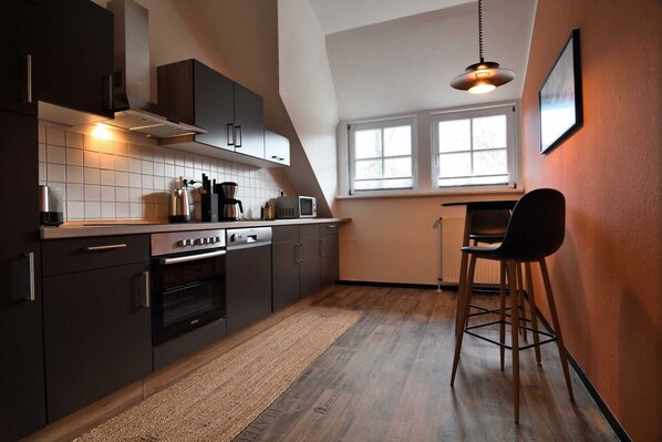 Una cocina moderna con armarios oscuros, horno empotrado y ventana que proporciona luz natural.
