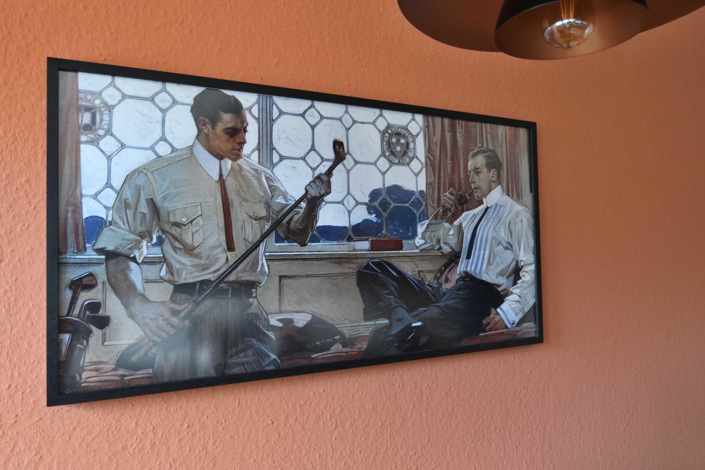 A framed artwork depicting two men in a room with a window and a desk.