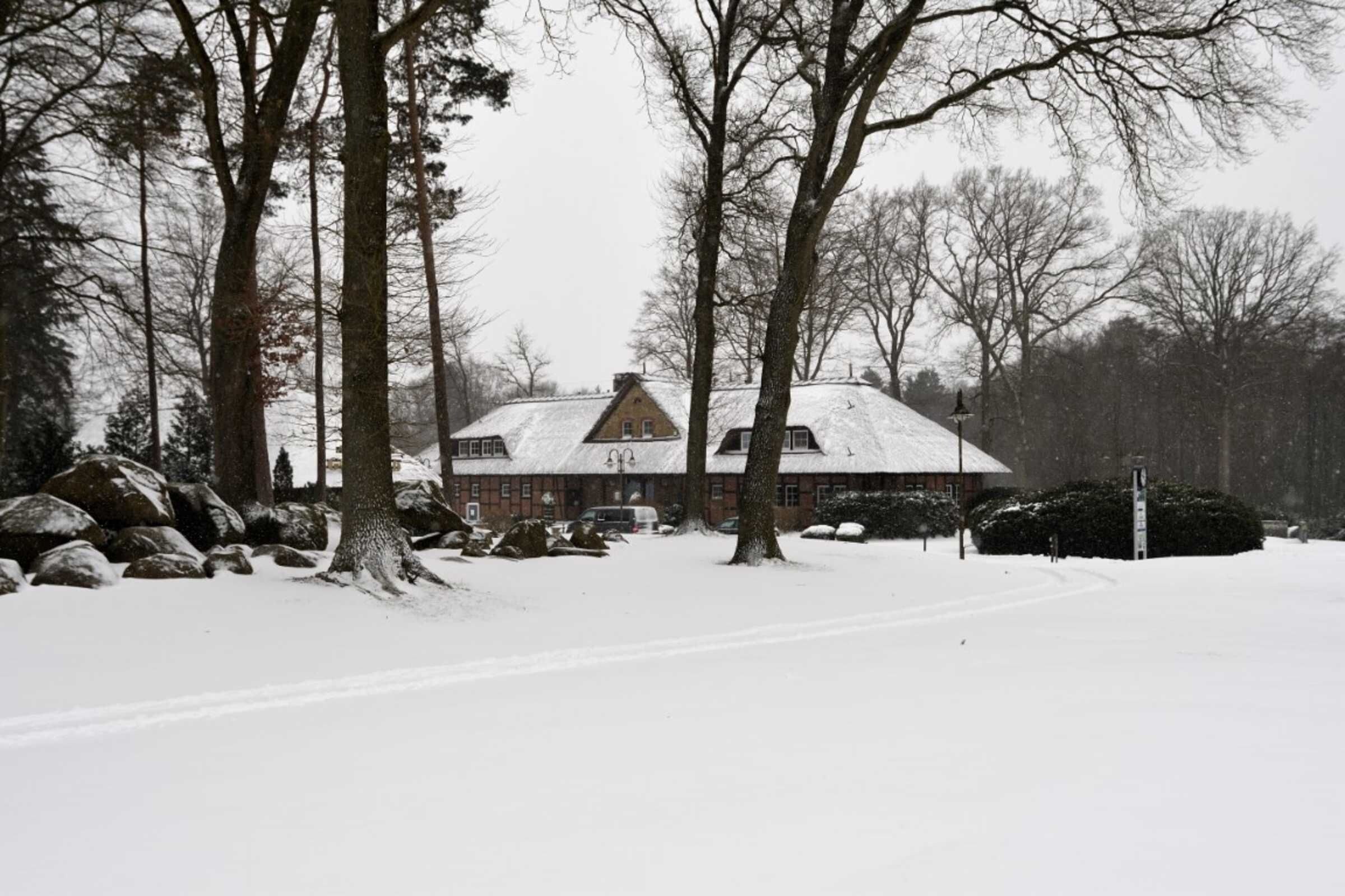 A snow-covered landscape with a large house surrounded by trees and rocks.