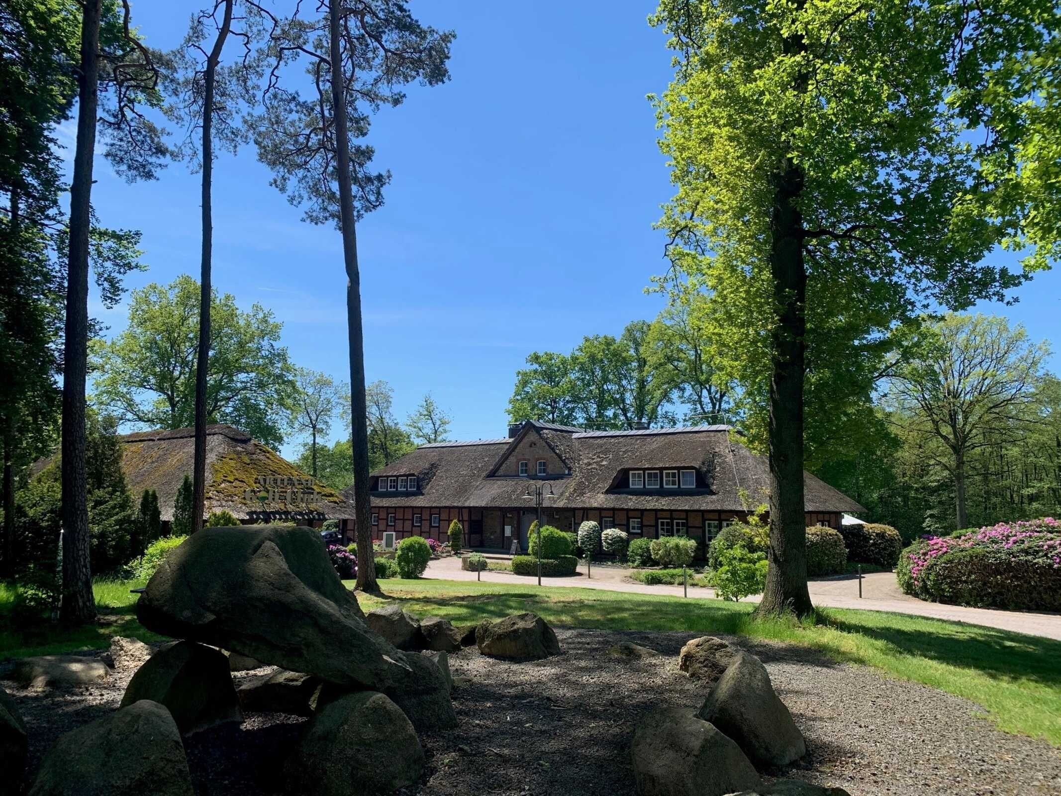 A large, traditional building with a thatched roof, surrounded by a well-maintained garden with large rocks and trees.