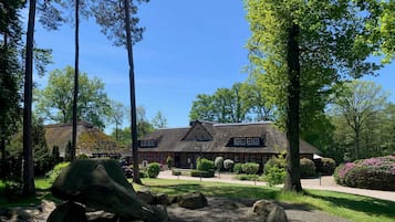 A large, traditional building with a thatched roof, surrounded by a well-maintained garden with large rocks and trees.