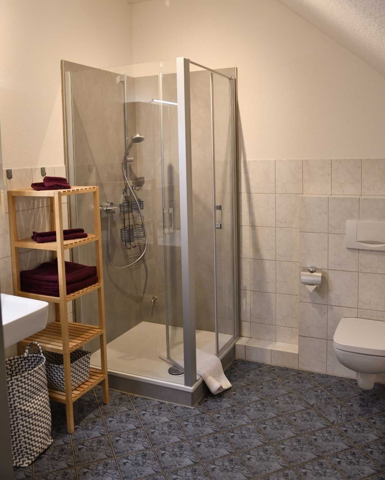 Ein Badezimmer mit einer Duschkabine, einem Holzboden mit Handtüchern, einem Waschbecken und einer Toilette.