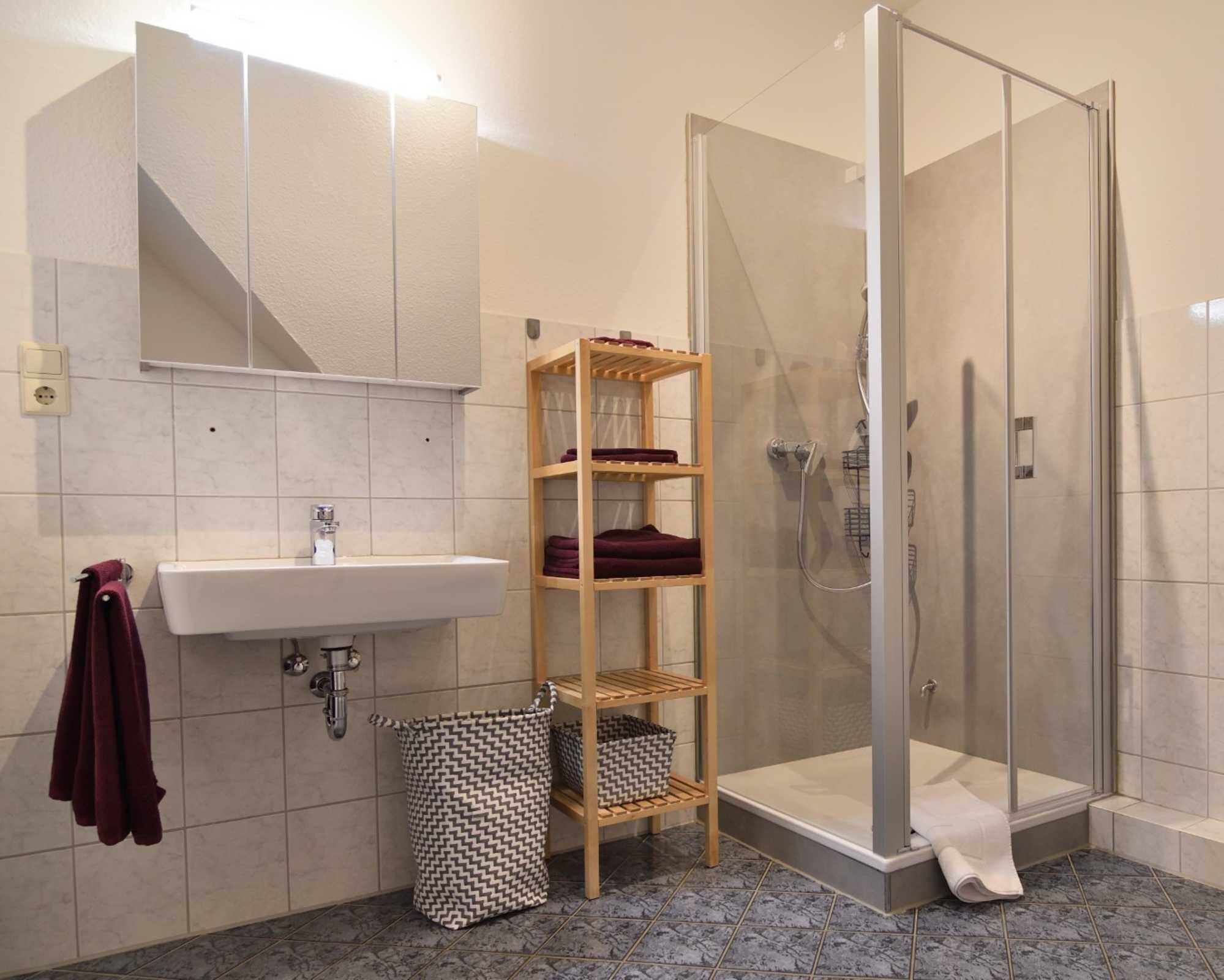 Ein Badezimmer mit Waschbecken, Spiegel, Dusche und einem Holzboden mit Handtüchern.
