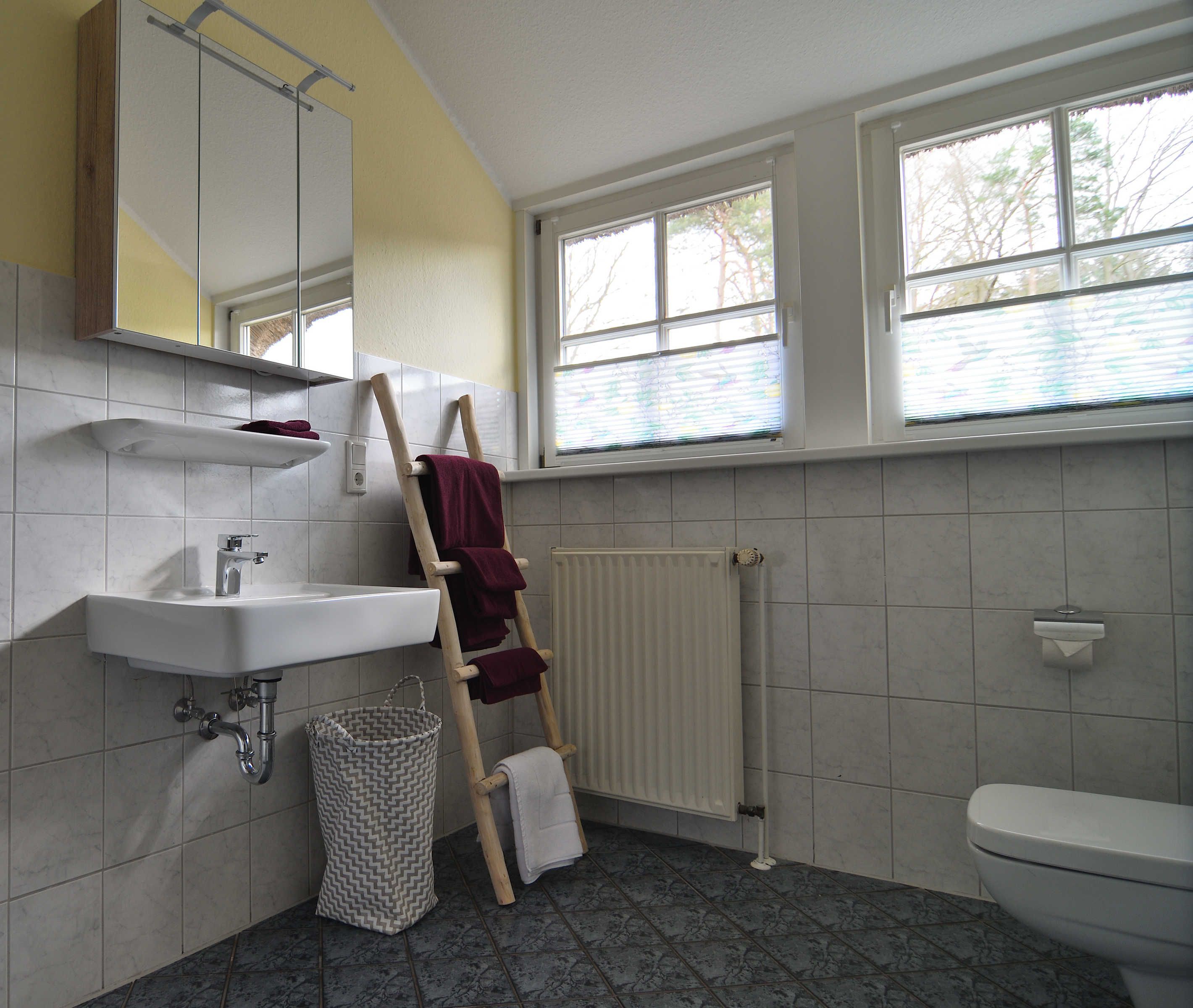 Ein Badezimmer mit weißem Waschbecken, Spiegel und Toilette, einem Holzhandtuchhalter und einer Heizung.