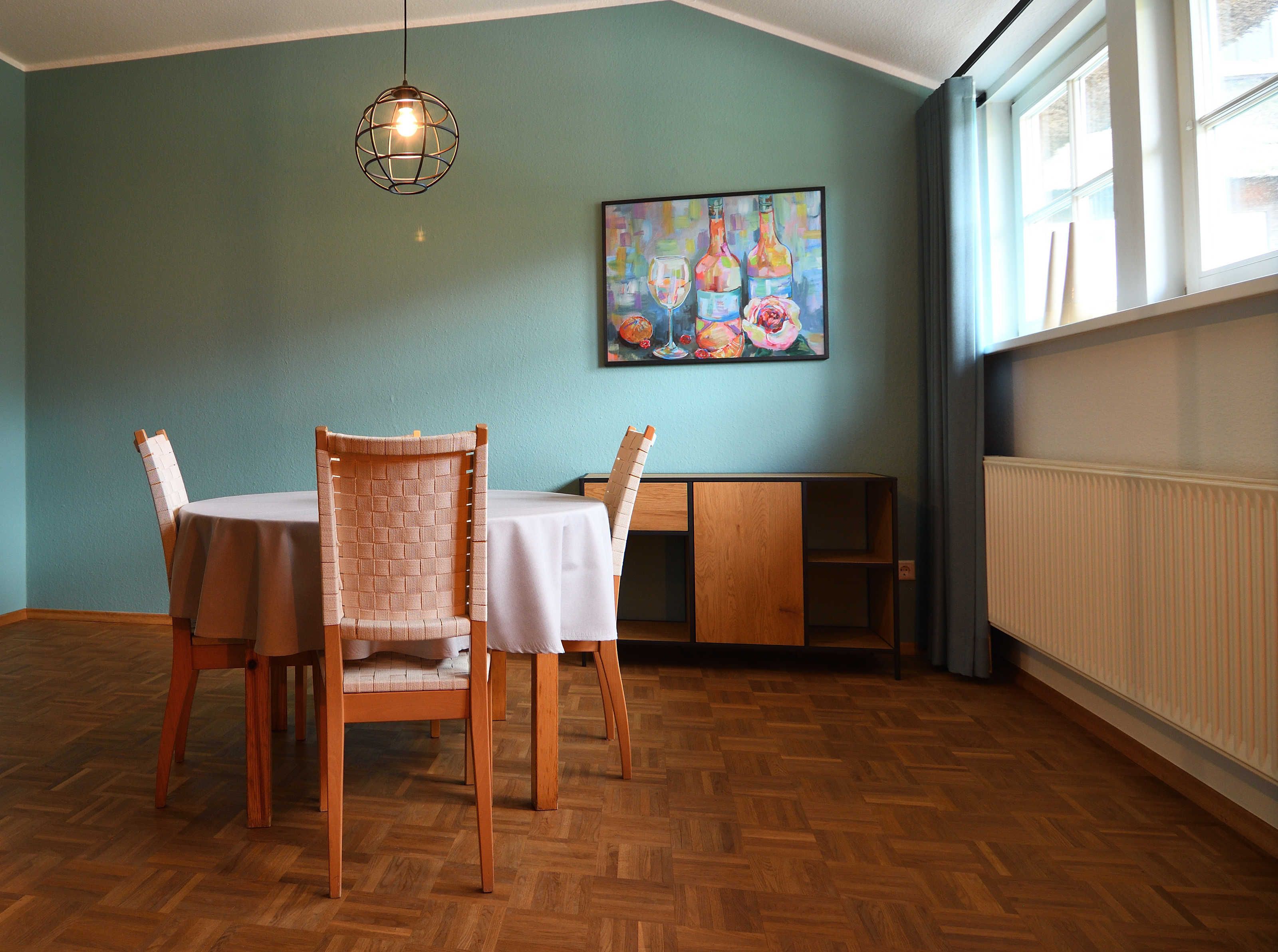 A dining area with a table and chairs, a painting on the wall, and a radiator.