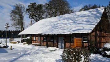 A traditional wooden building with a snow-covered roof, a wooden bench, and a small garden area.